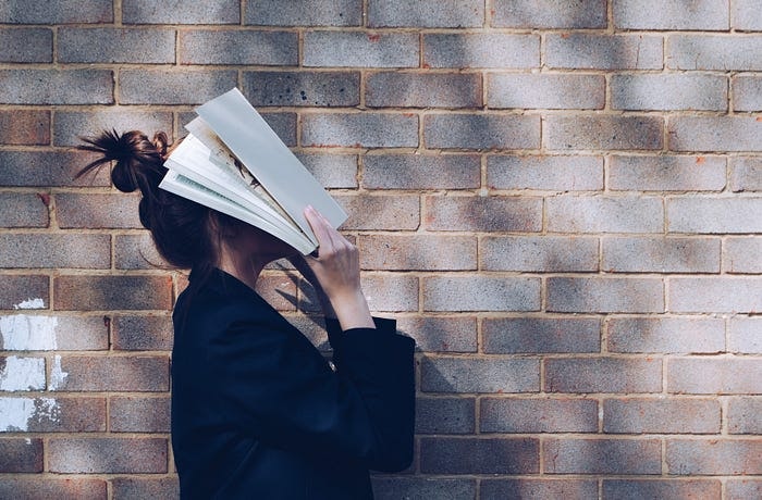 壁の前で本で彼女の顔を覆っている